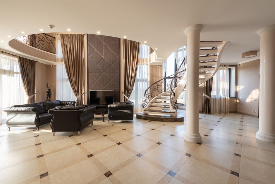 Interior of spacious hallway of classic styled villa with columns and comfortable leather sofa and armchair placed near spiral staircase
